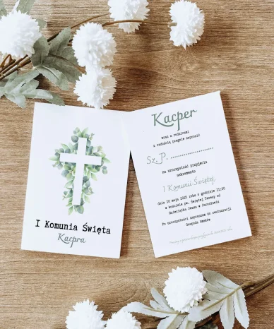 Elegancka karta zaproszenia na I Komunię Świętą z motywem krzyża i białymi kwiatami na drewnianym tle.