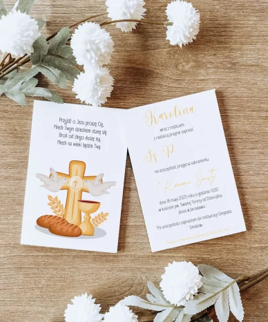 Zaproszenie na I Komunię Świętą z motywem krzyża, kielicha i gołębi, udekorowane białymi kwiatami na drewnianym tle.